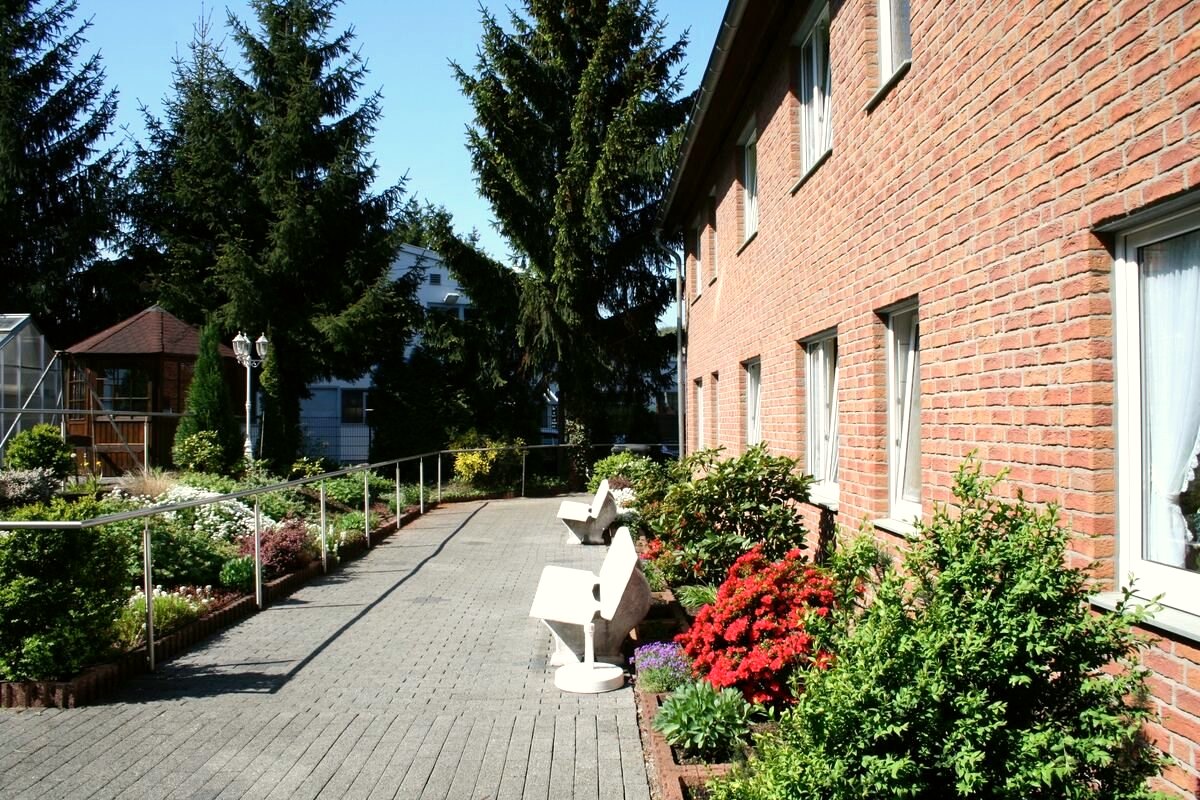 Sonnige Terrasse an der Gartenseite mit Sitzbänken, Beeten und blühenden Sträuchern